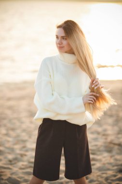 Nehir kıyısındaki uzun saçlı sarışın. Mutlu genç kız bir sonbahar gününde rahatlar.