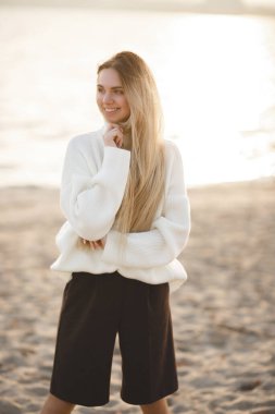 Nehir kıyısındaki uzun saçlı sarışın. Mutlu genç kız bir sonbahar gününde rahatlar.