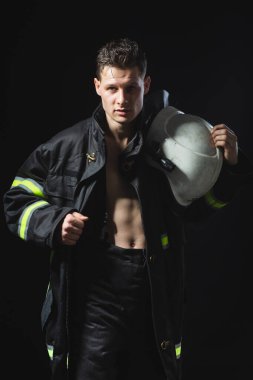 Fashionable portrait of a young man in fire equipment on a black studio background. Fireman in a dark uniform clipart