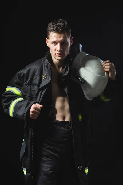 黒のスタジオの背景にある消防機器の若い男のファッショナブルな肖像画 暗い制服を着た消防士 — ストック写真