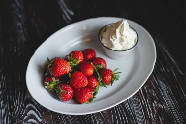 Kremalı çilek. Yemek fotoğrafçılığı. Koyu ahşap arka planda iştah açıcı çilekler.