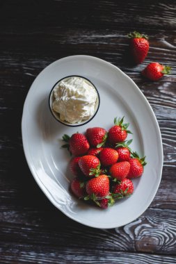 Kremalı çilek. Yemek fotoğrafçılığı. Koyu ahşap arka planda iştah açıcı çilekler.