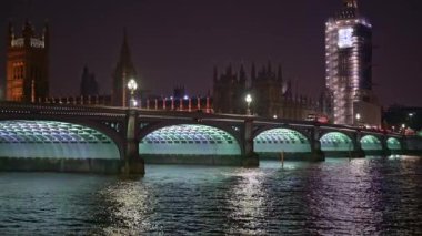 Kırmızı çift katlı otobüsler gece Westminster Köprüsü 'nden geçiyor. Arka planda Parlamento Binaları.