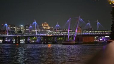 Thames Nehri 'nin karşısındaki Altın Jübile Köprüleri. İnsanlarla dolu ve gece bir tren geçiyor.