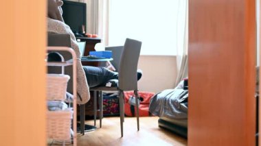 Düşük açılı kayma resmi, başlıklı sabahlık giymiş bir kadının masada dizüstü bilgisayarda çalıştığını gösteriyor..