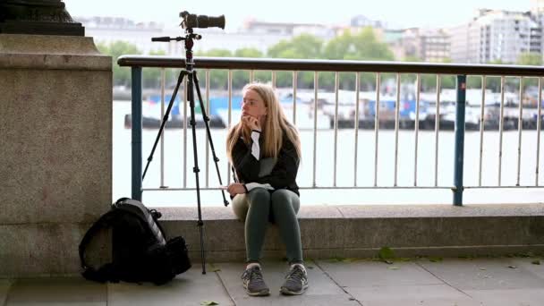 ロンドン 2021年5月31日 川沿いのカメラと三脚の横に座っている間 退屈した女性写真家の笑顔 — ストック動画