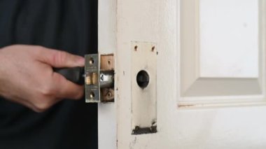 Bir adamın elleri eski bir kapı kilidini açmak için tornavida kullanır.