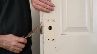 Bir adamın elleri paslı bir keski kullanarak kapı kilidi namlusunu genişletir.