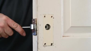 Bir adamın elleri kapı kilidini açmak için bir tornavida kullanır.