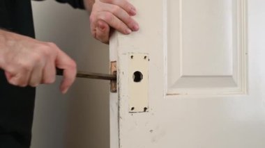 Bir adamın elleri, kapı kilidi namlusunu genişletmek için bir dosya kullanır.