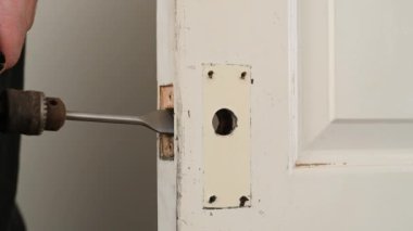 Bir elektrikli matkap, kapı kilidi namlusuna delik açıyor. Beyaz, eski bir iç kapıda.