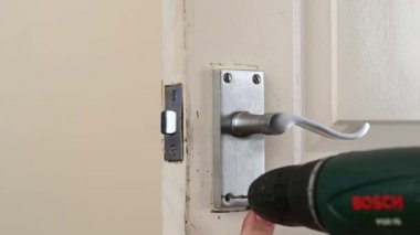 Richmond, Kuzey Yorkshire, İngiltere - 18 Kasım 2021: Yaşlanmış beyaz bir iç kapıya yeni bir kapı kolu takmak için elektrikli matkap kullanmak
