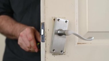 Yeni kapı kollarını sıkmak için tornavida kullanan bir adamın elleri odak dışı.