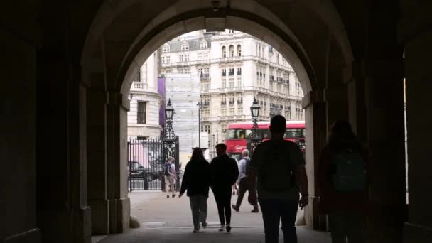 ロンドン 2022年5月18日 背景に赤いロンドンのダブルデッキバスと馬のガードパレードへの入り口のアーチを歩くシルエットの人々 — ストック動画