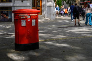 LONDON - May 16, 2022: Traditional British red Postbox with people passing by in the background