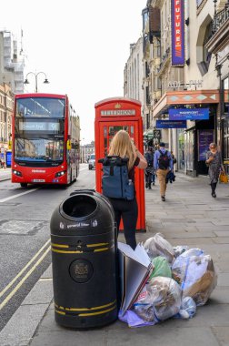 LONDON - May 18, 2022: Litter, a red Double Decker bus and a traditional British Telephone box outside Adelphi Theatre, London