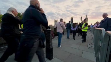 14 Eylül 2022 'de Westminster Köprüsü' ndeki bir güvenlik kontrol noktasından geçmek için Kraliçe 'nin bilekliklerde yattığını görmek için kuyruk oluştu. Parlamento binaları gün batımında arka planda