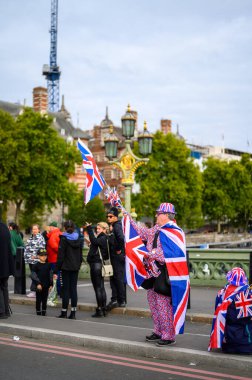 Londra - 19 Eylül 2022: Union Jack bayrak takımı ve şapka giyen adam Westminster Köprüsü 'nde Union Jack hediyelik eşya satıyor