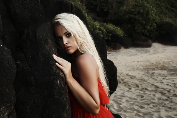 Beautiful blond woman near a rock on the beach — Stock Photo, Image