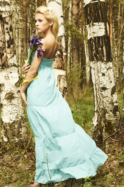 Hermosa mujer rubia con flores azules caminando en un bosque —  Fotos de Stock