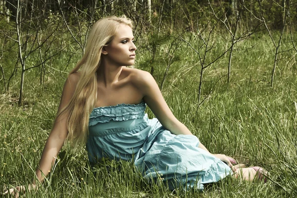 Красивая блондинка сидит на зеленой траве — стоковое фото