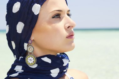 Beautiful woman in a blue scarf on the beach clipart