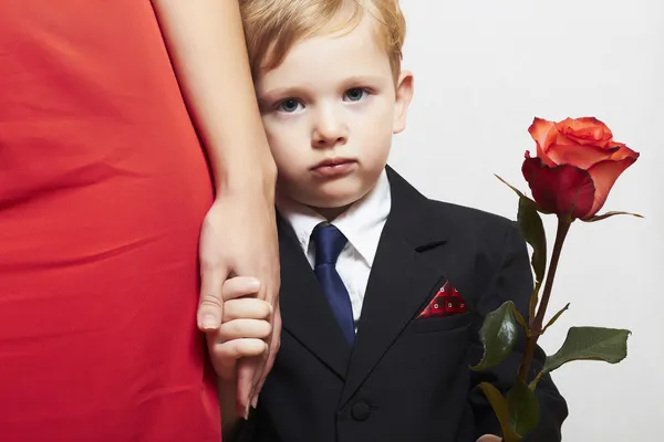 Barn i kostym med mamma. blomma. röd klänning. familj. fashionabla liten pojke. röd ros. ta hand — Stockfoto