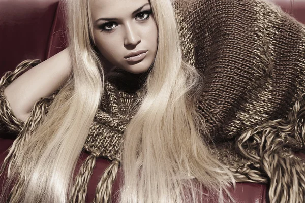 Mooie blonde vrouw op rood lederen sofa. schoonheid mode meisje in poncho — Stok fotoğraf