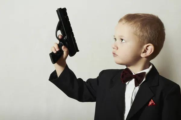 El pequeño James Bond. Muchacho de moda en corbata de moño. Niños de moda. Niño de 4 años con traje negro. Elegancia chico guapo con pistola . — Foto de Stock