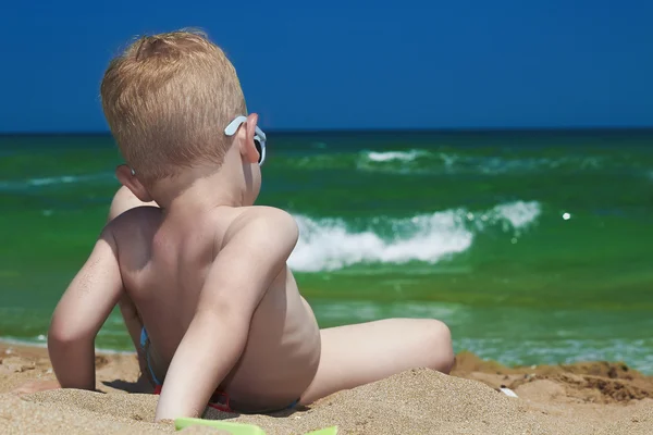 Malý chlapec na pláži. dítě sedí v písku. Při pohledu na moři. léto. zelené moře. modrá obloha — Stock fotografie