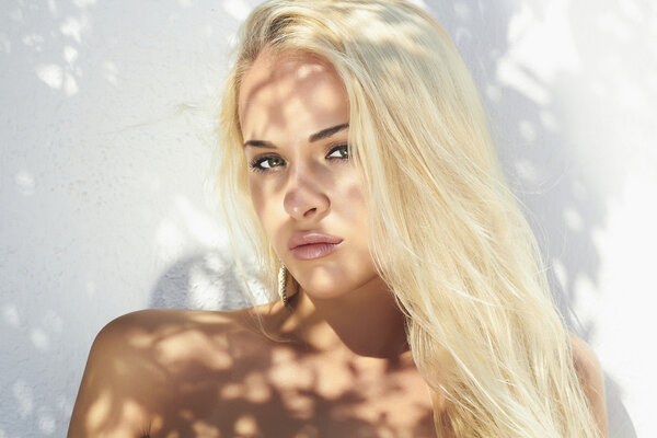 Beautiful blond woman in daylight. real shadows on the face.girl near white wall