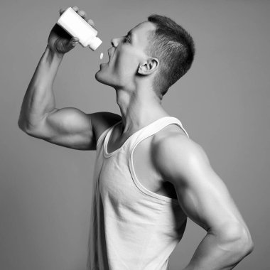 Vücut geliştirici haplar, steroidler. Şişeli yakışıklı fitness çocuğu. Vücut kaslı spor adamı. Spor beslenmesi. Siyah beyaz portre