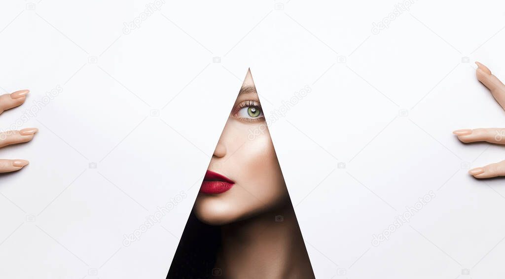 young beautiful woman with a bright makeup. make-up artist concept. A girl with beautiful bright green eyes with shining shadows, looks into the hole of white paper