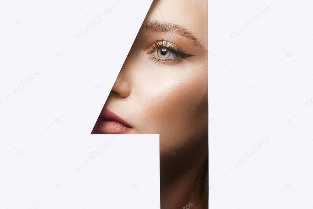 young beautiful woman. make-up artist concept. A girl with beautiful bright green eyes with shining shadows, looks into the hole of white paper. number one