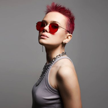 Kısa boyalı saçları ve kırmızı gözlüklü zincirli kolyesi olan güzel bir kadın. Mücevherli güzel seksi manken kız. Pembe Saç Tarzı