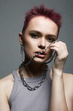 Genç ve güzel bir kadın, kısa saçlı ve ağzında zincirli kolyesi var. Mücevherdeki eski model kız. Pembe Saç Tarzı