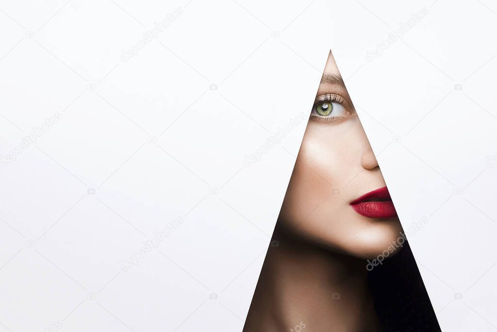 young beautiful woman with a bright makeup. make-up artist concept. Pretty girl looking into the hole of white paper