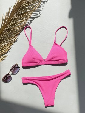 Beton zeminde pembe mayo ve güneş gözlüğü var. Yazlık giysiler. mayo, bardak ve palmiye yaprakları