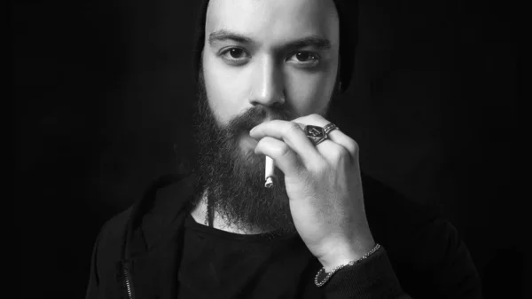 handsome bearded smoking man in Hat. Hipster boy with cigarette, black and white portrait