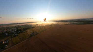 Black and orange hot air balloon floating above field, beautiful summer sunrise. Dynamic aerial shot. High quality 4k footage