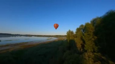 FPV drone maneuvers up and down around Black and orange hot air balloons floating above lake. Dynamic aerial shot. High quality 4k footage