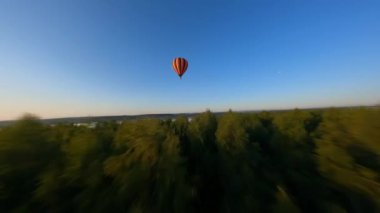 FPV drone maneuvers up and down around Black and orange hot air balloons floating above lake. Dynamic aerial shot. High quality 4k footage