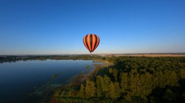 Drone orbiting close to black and orange hot air balloon, reveal of sunshine in the morning above beautiful rural area.