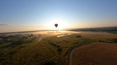 Beautiful acrobatic aerial shot of hot air ballon floating above sloping field, sunny morning in Russia