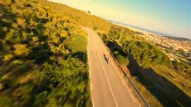Fast motorcycle riding on serpentine road filmed with fpv drone on high speed during golden hour, driver with white long sleeve shirt . High quality 4k footage