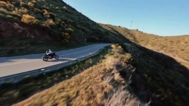 Fast motorcycle riding on serpentine road during golden hour, driver with white long sleeve shirt . followed with high speed fpv drone, Slowmo 4k footage