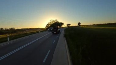 Cinematic FPV shot of Gray Stylish landrover with motorcycle on the back driving on the green field road during beautiful sunset. High quality 4k footage