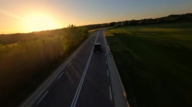 Cinematic FPV shot of Gray Stylish landrover with motorcycle on the back goes on the green field road during sunset. High quality 4k footage