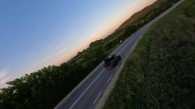 Dynamic aerial shot of Gray Stylish suv with motorcycle on the back driving on the green field road 