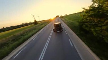 Cinematic FPV shot of Gray Stylish landrover with motorcycle on the back driving on the green field road during beautiful sunset. High quality 4k footage